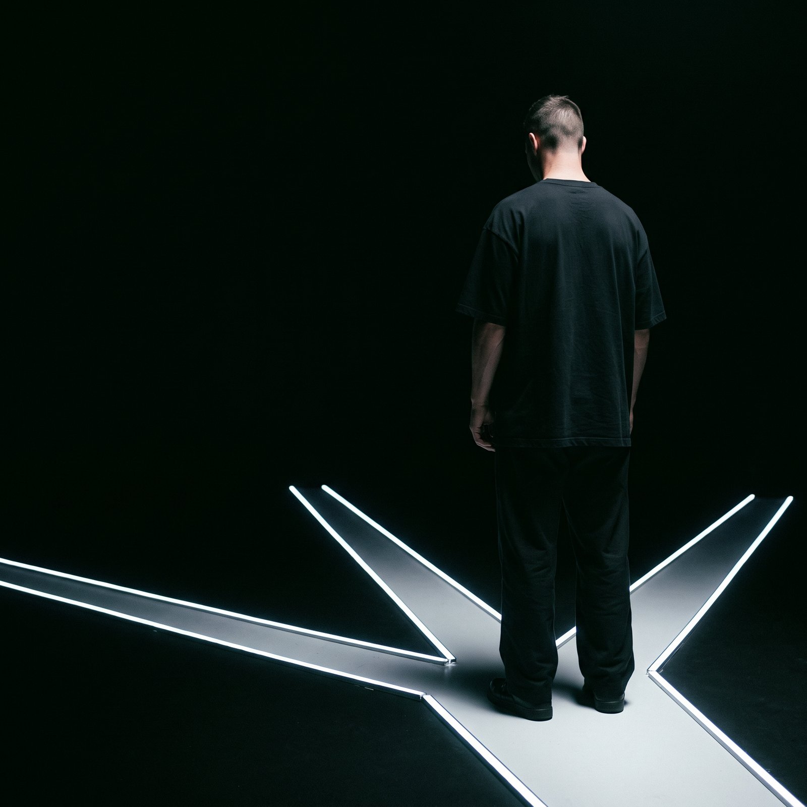 A man seen from behind stands where glowing white lines on a black floor split into several paths.